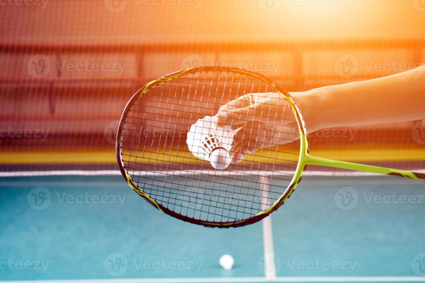 la raqueta de bádminton y el viejo volante blanco sosteniéndose en las manos del jugador mientras lo sirven sobre la red por delante, desdibujan el fondo de la cancha de bádminton y el enfoque selectivo foto