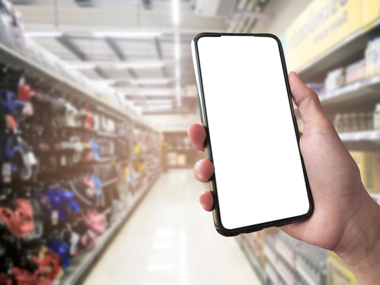 concepto de compra inteligente teléfono móvil en la mano frente a estantes de productos en supermercados y tiendas de comestibles. maqueta de pantalla blanca en blanco para su propia creatividad. foto