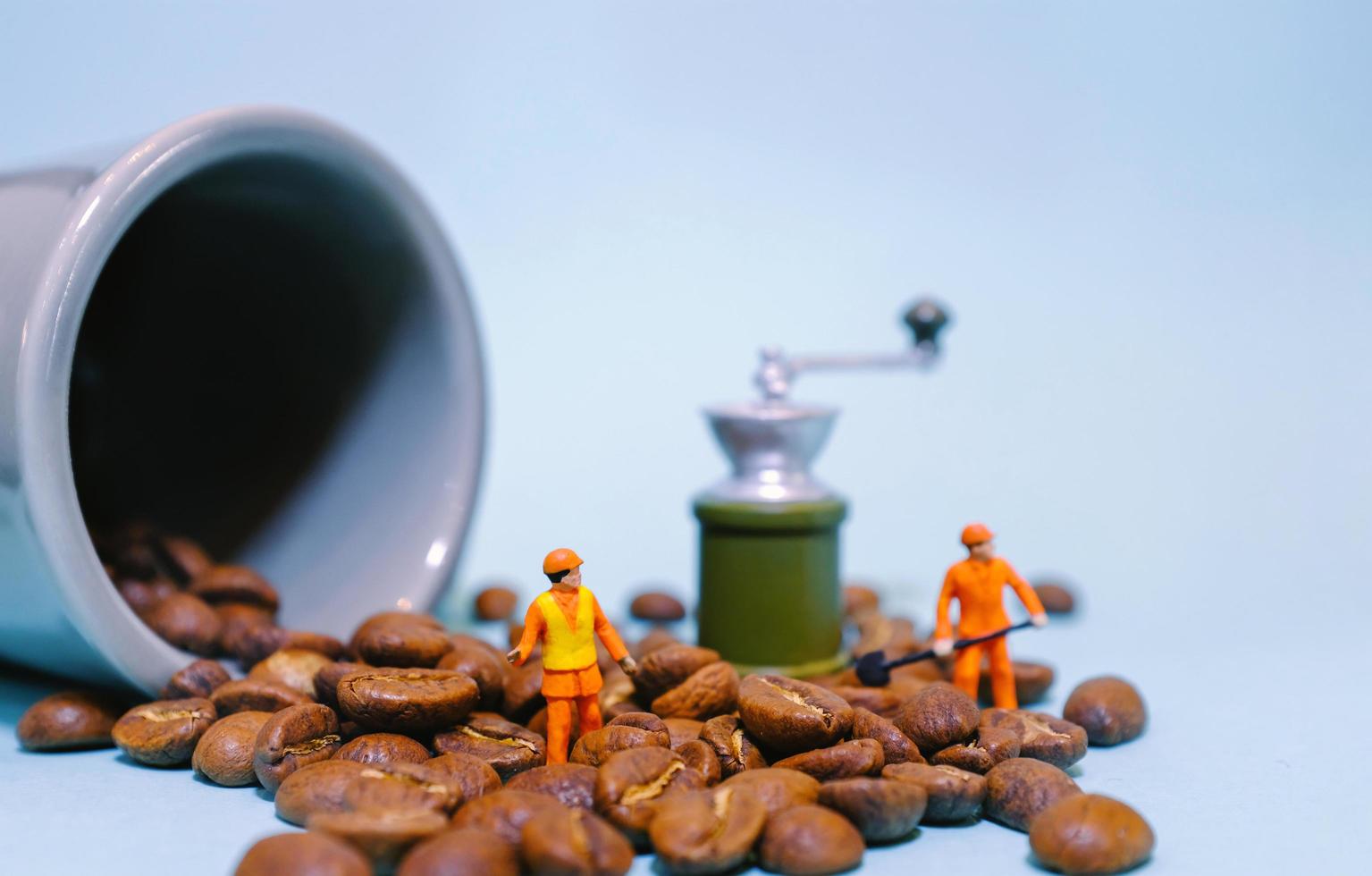 Miniature people worker on coffee beans with cup and grinder machine, food and drink concept photo