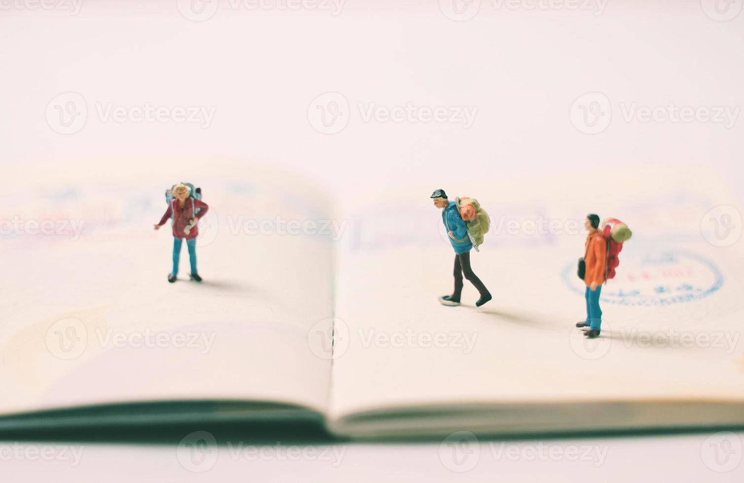 Miniature people figures with backpack walking and standing on passport page with immigration stamps, travel and vacation concept photo