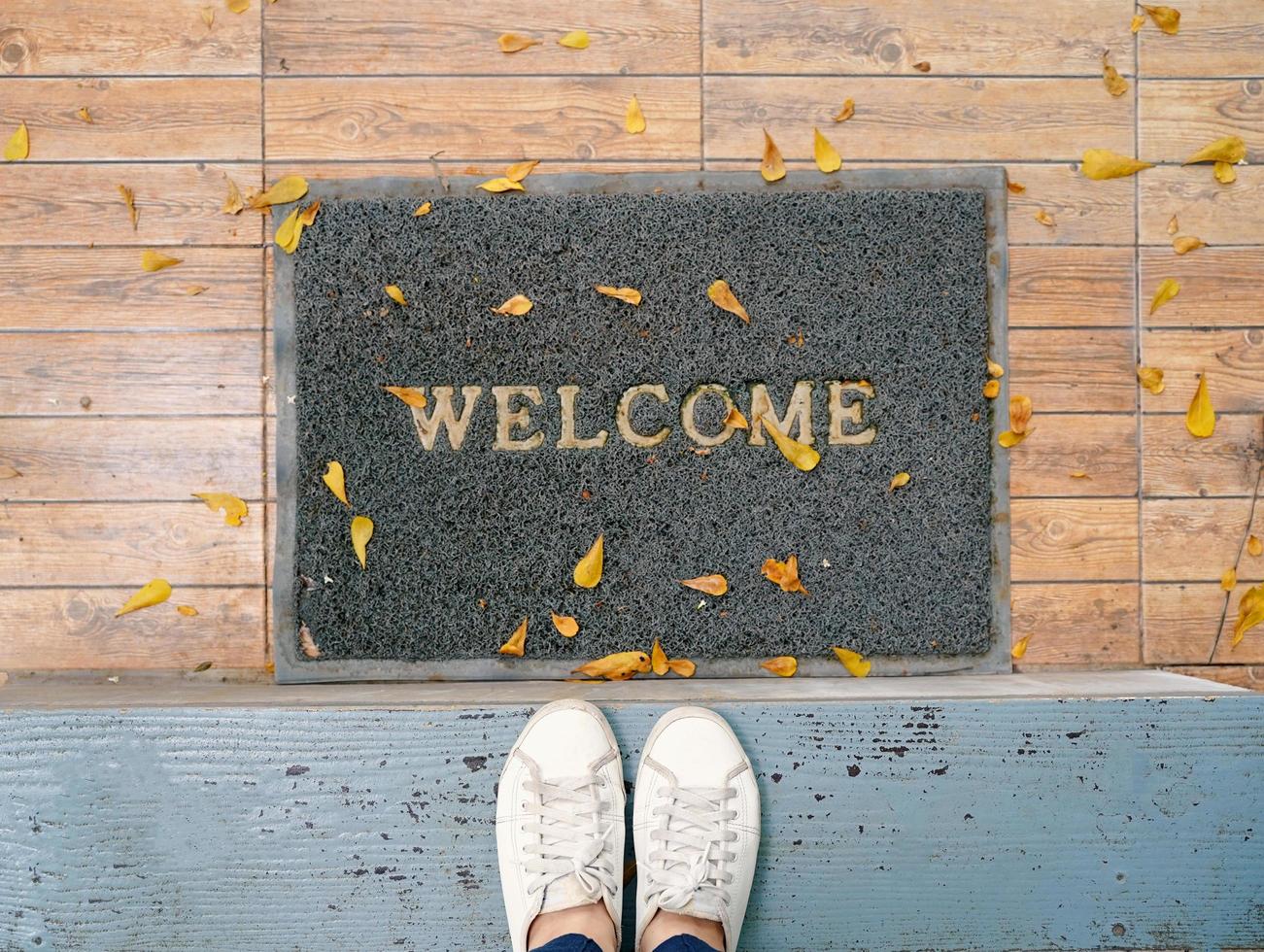 Top view selfie of feet in white sneakers shoes on floor background with welcome mat photo
