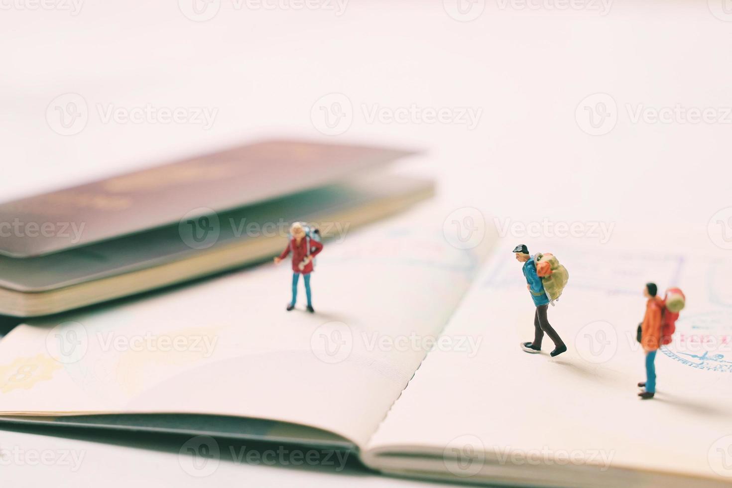 Miniature people figures with backpack walking and standing on passport page with immigration stamps, travel and vacation concept photo