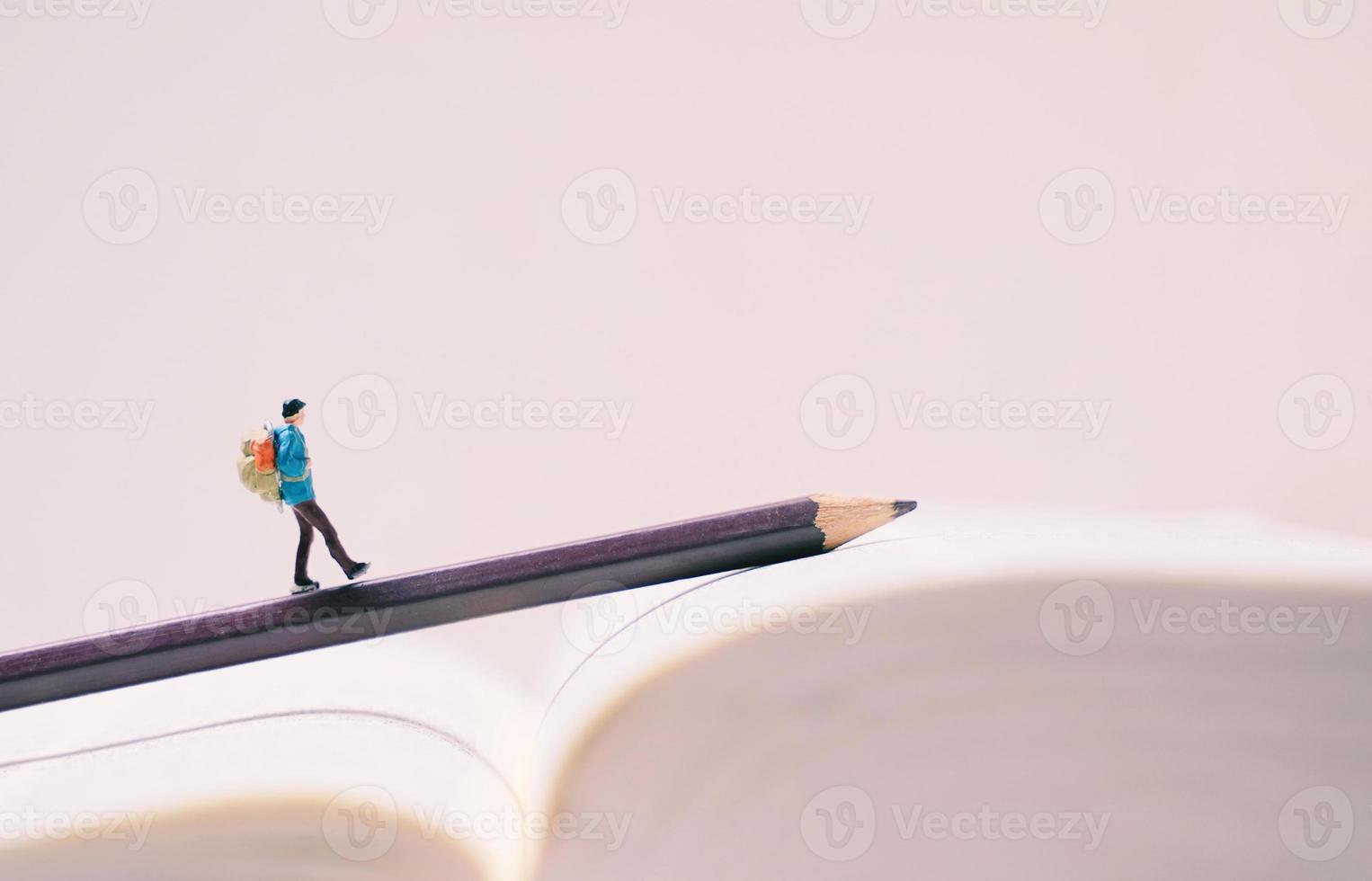 Miniature people figures with backpack walking on pencil and book with copy space, travel and study abroad concept photo