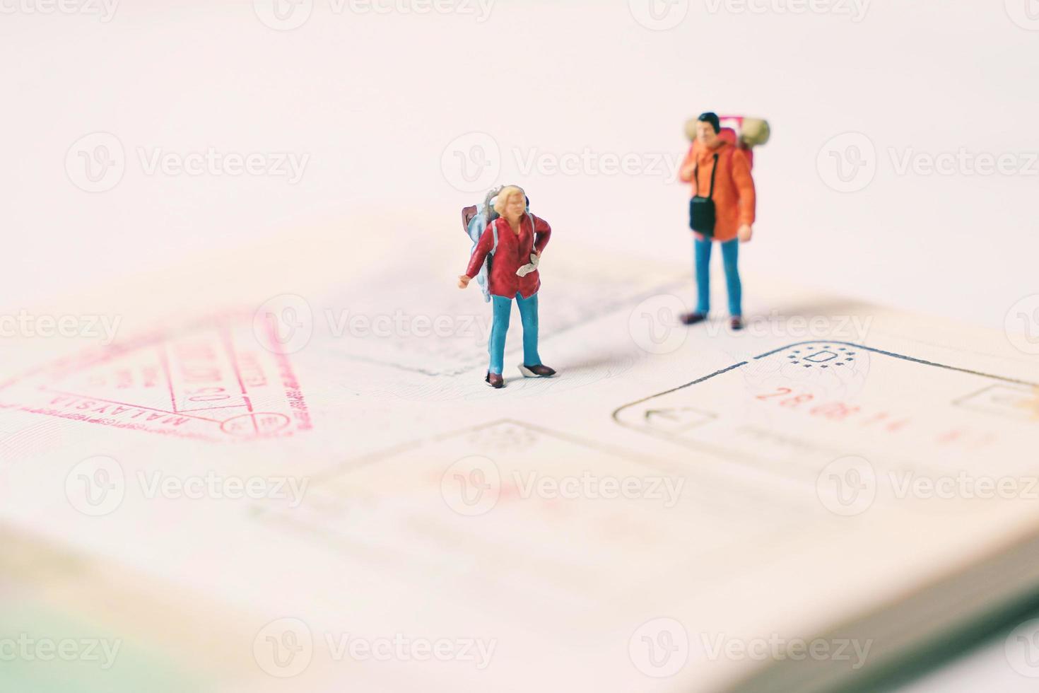 Miniature people figures with backpack walking and standing on passport page with immigration stamps, travel and vacation concept photo