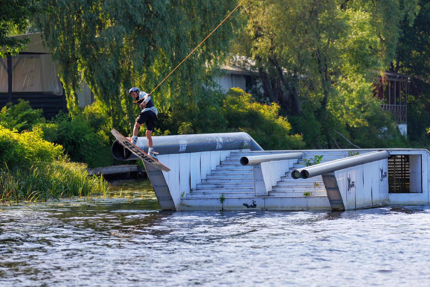 Kyiv. Ukraine. Jun.19, 2022. Athlete wakeboarder jumps from a springboard to the water surface on a summer day. photo