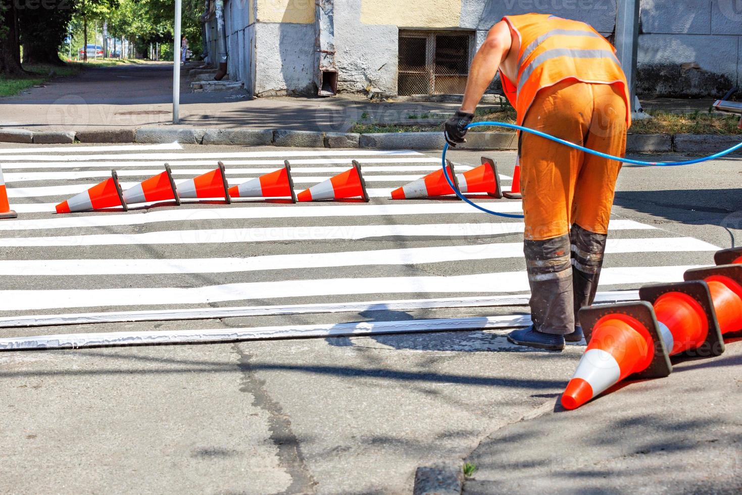 A road worker paints with an airbrush the markings of a pedestrian crossing on a roadway on a sunny day. photo