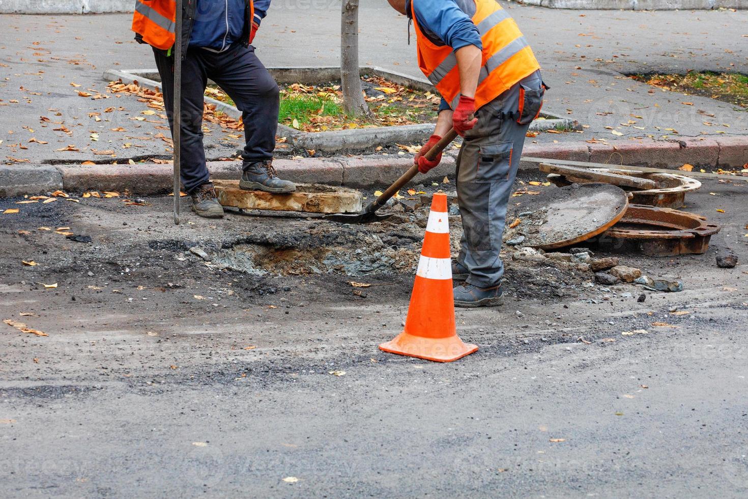 A team of road workers with a shovel and iron crowbar is repairing a sewer hatch on the roadway. photo