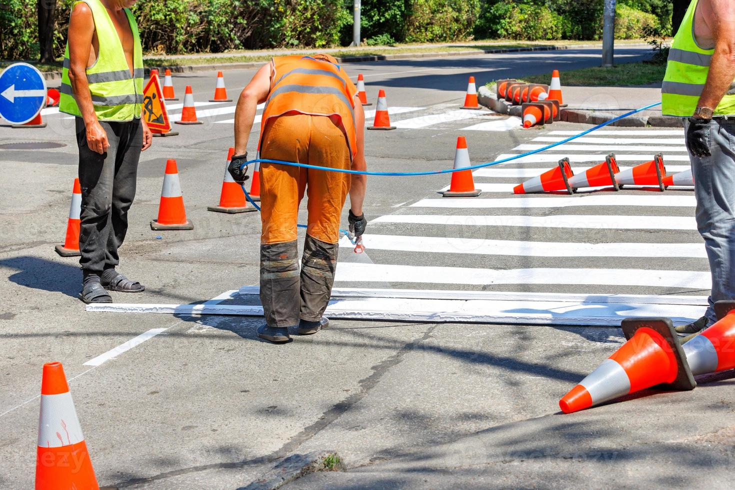 A team of road workers mark a pedestrian crossing on the roadway with white paint. photo