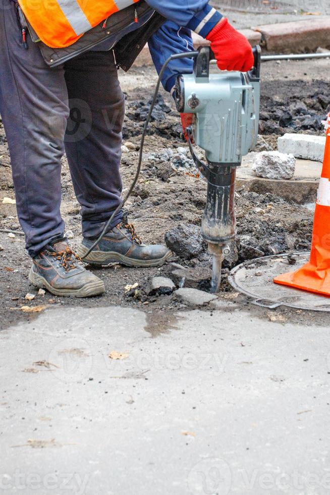 A worker using an electric jackhammer destroys the old asphalt near the sewer manhole. photo