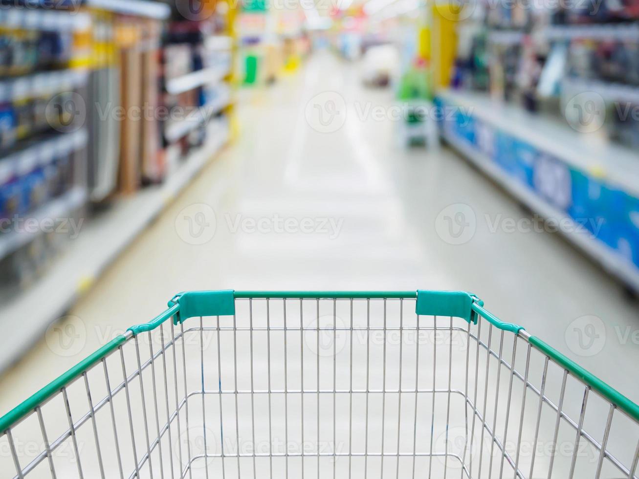 Supermarket aisle with empty green shopping cart blurred background photo