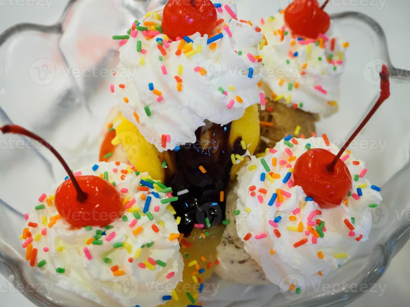 Ice cream sundae scoops with cherry and whipped cream in glass bowl photo