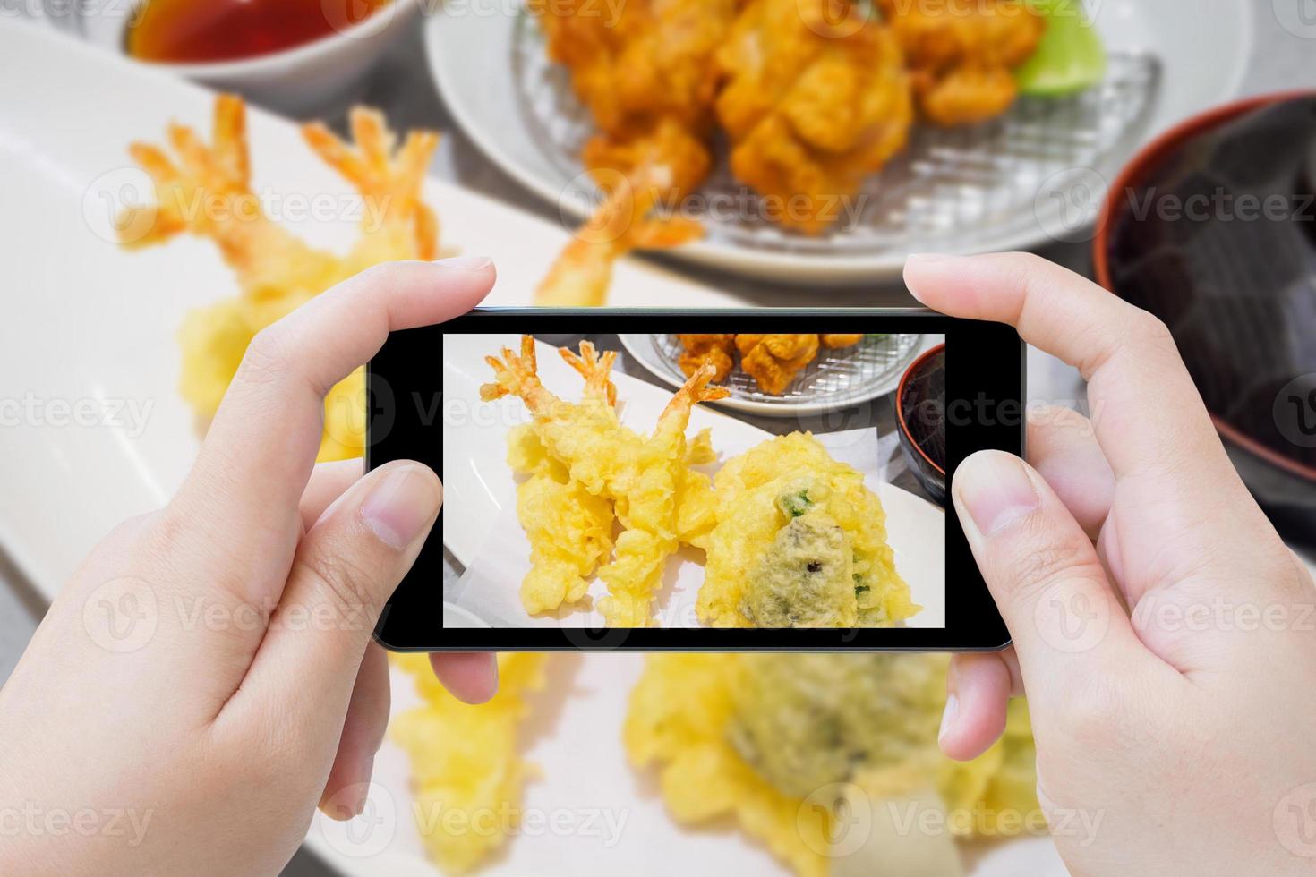 tomando una foto de tempura de camarones en un plato blanco con un teléfono inteligente