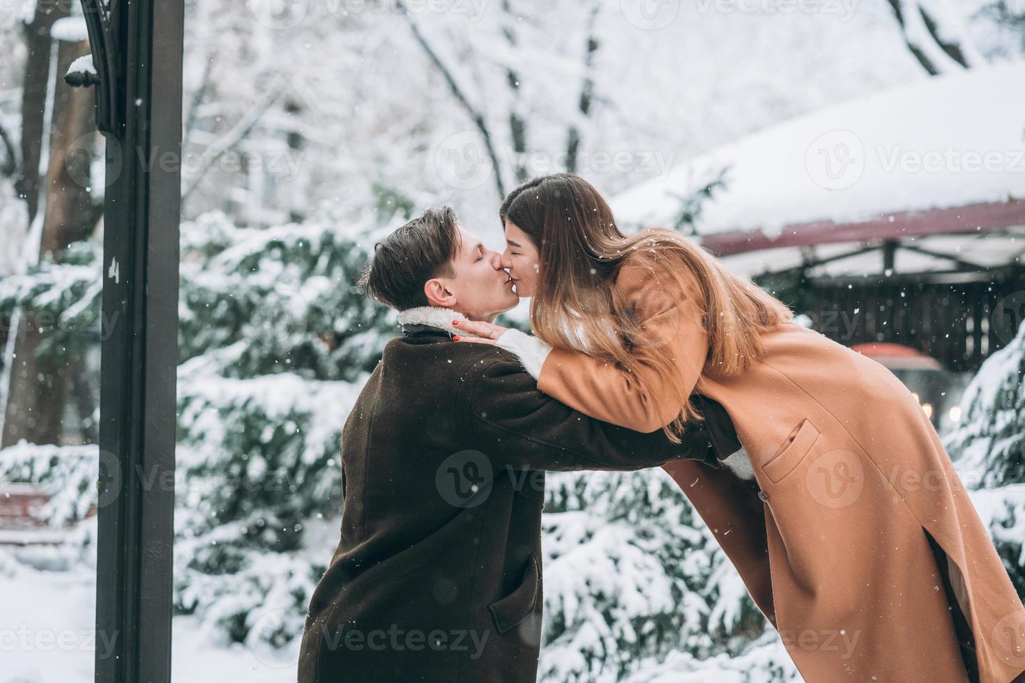 young guy and beautiful girl kiss in a snowy park photo