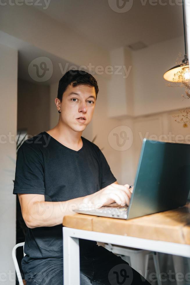 retrato de un hombre sentado en una mesa en casa trabajando en una laptop. foto