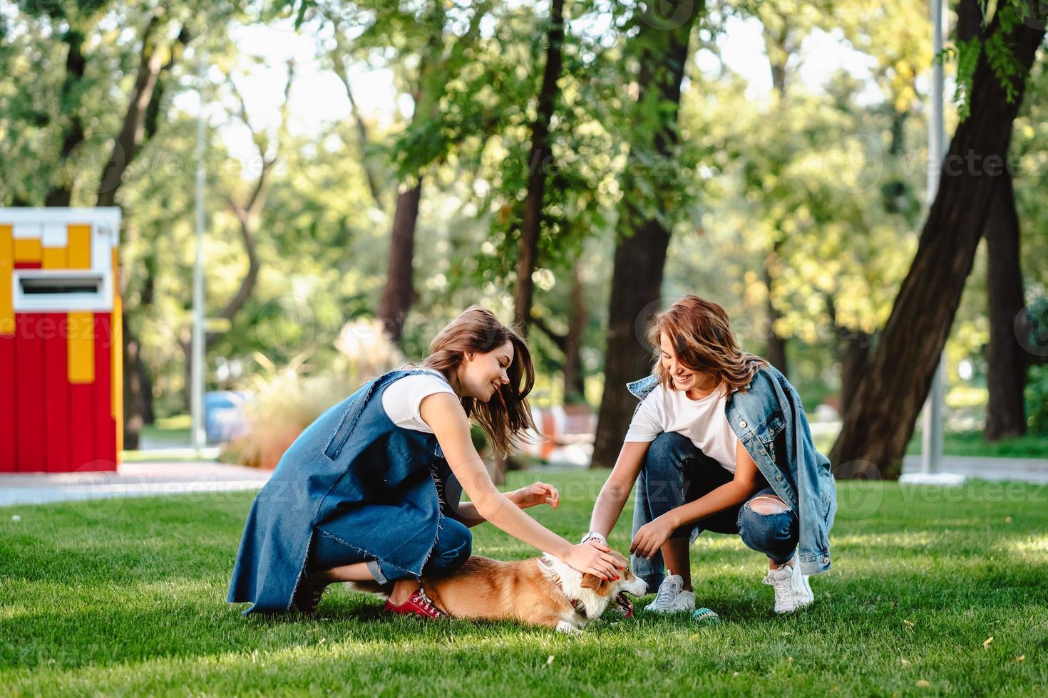 Two female friend in the park play with little dog photo