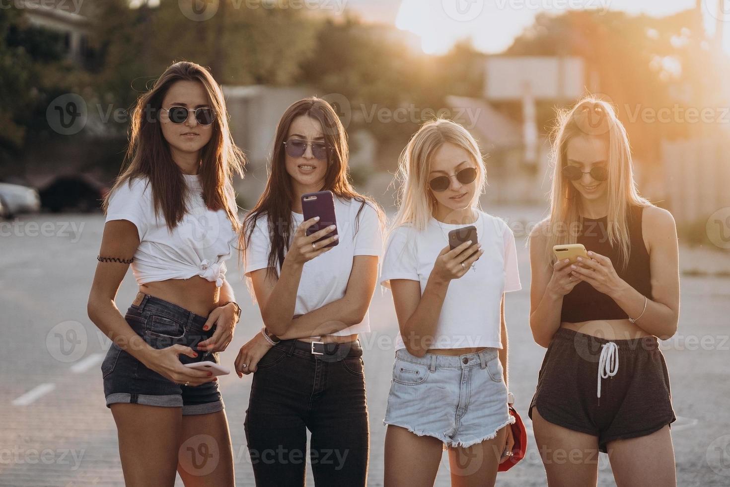 cuatro mujeres atractivas están de pie en el estacionamiento de automóviles con teléfonos inteligentes foto