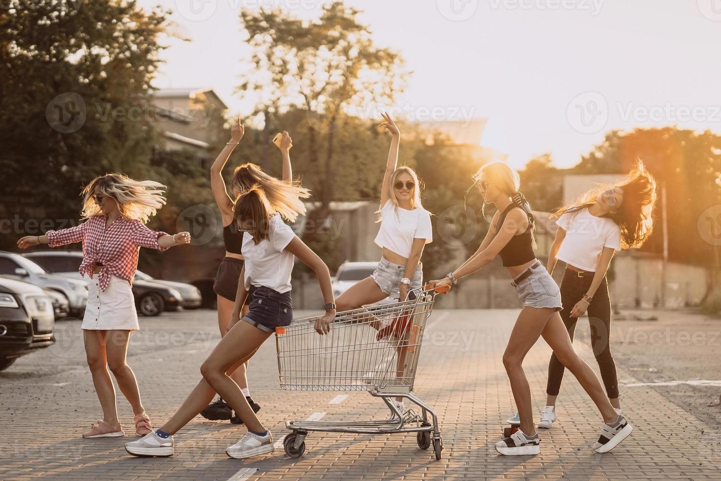 las mujeres jóvenes con un carrito de supermercado se divierten foto