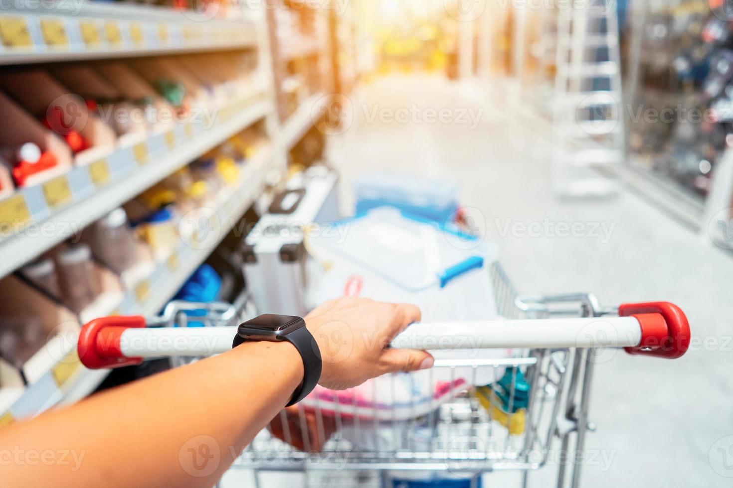 mano humana cerca con carrito de compras en un supermercado caminando por el pasillo foto