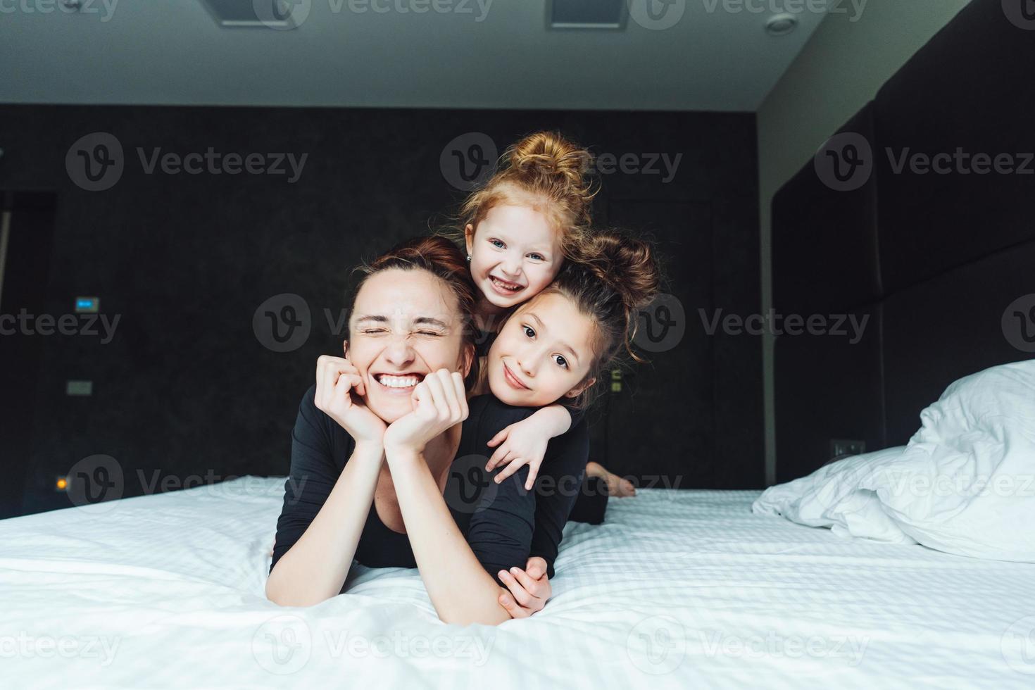 Mom and two daughters have fun on the bed photo