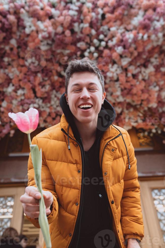 un hombre guapo tiene una flor, un tulipán rosa para su novia foto