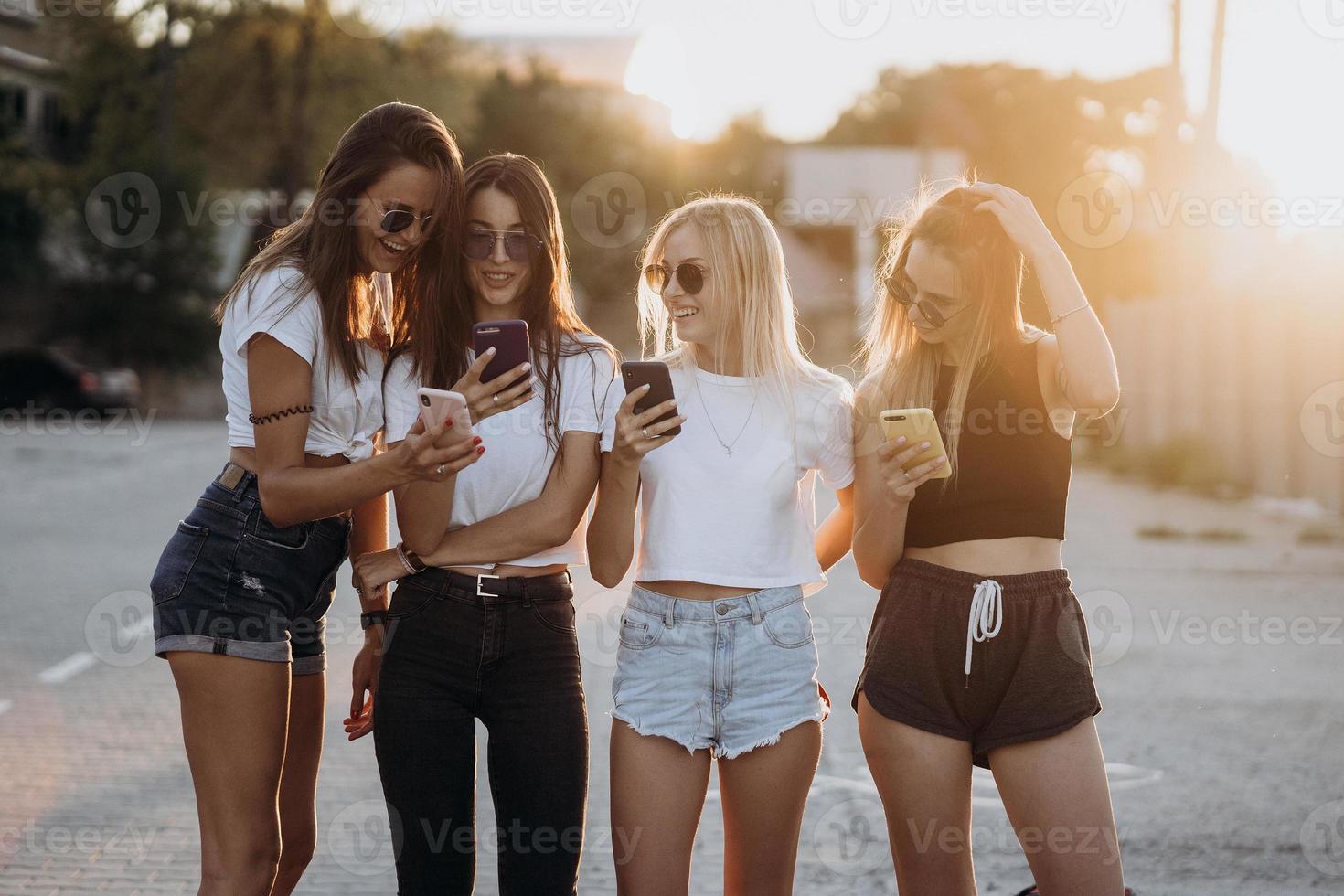 cuatro mujeres atractivas están de pie en el estacionamiento de automóviles con teléfonos inteligentes foto