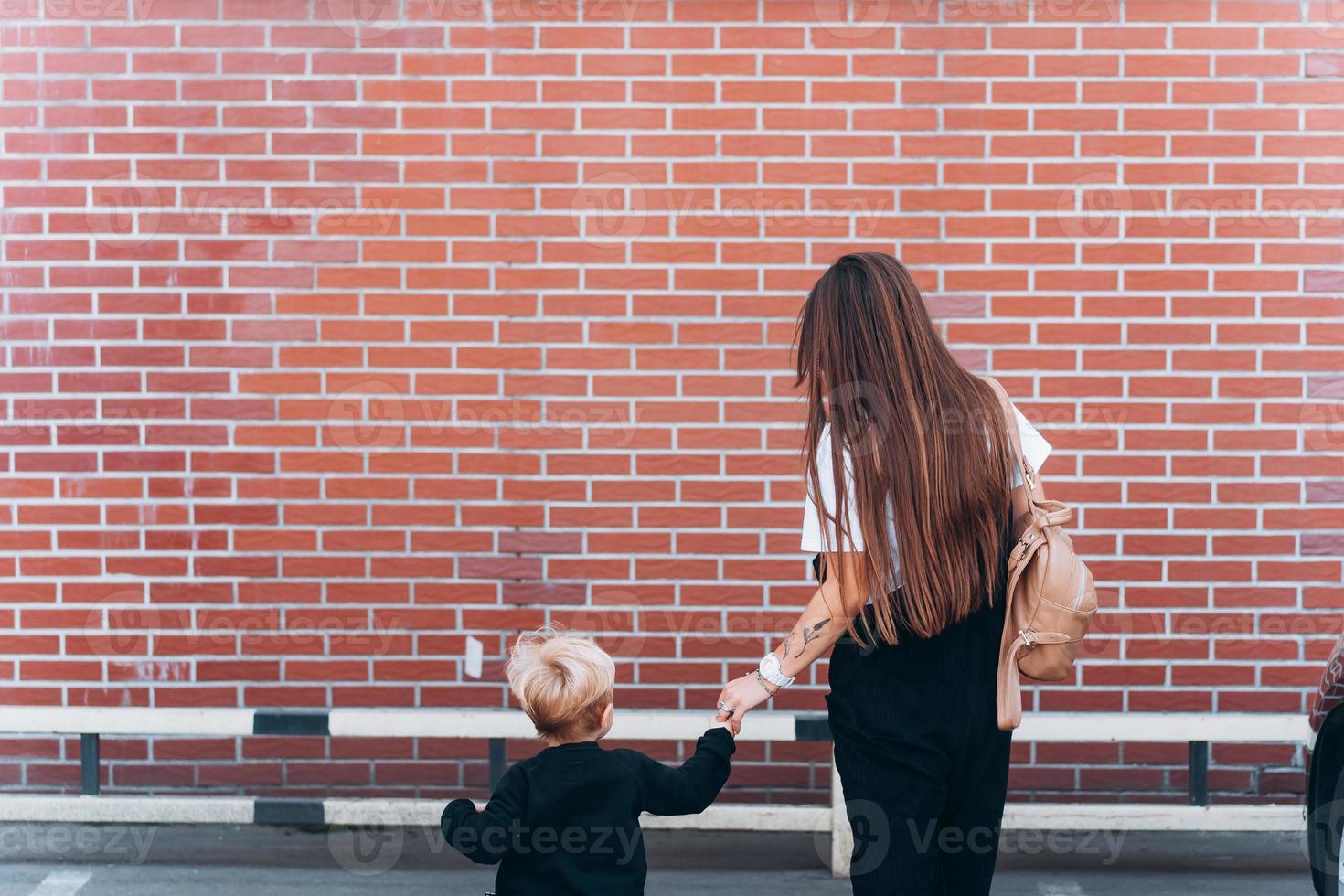 vista trasera de la madre y su pequeño hijo contra el telón de fondo de una pared de ladrillos foto