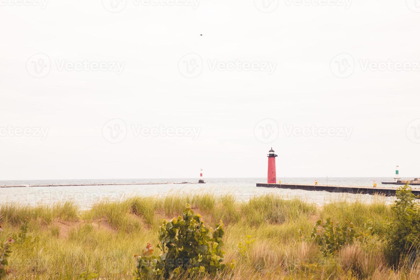 Lighthouse at end of pier on a cloudy windy day on Lake Michigan. Long pier. Dry grasses growing in the sand hills. Red and green buoys marking the harbor inlet. photo