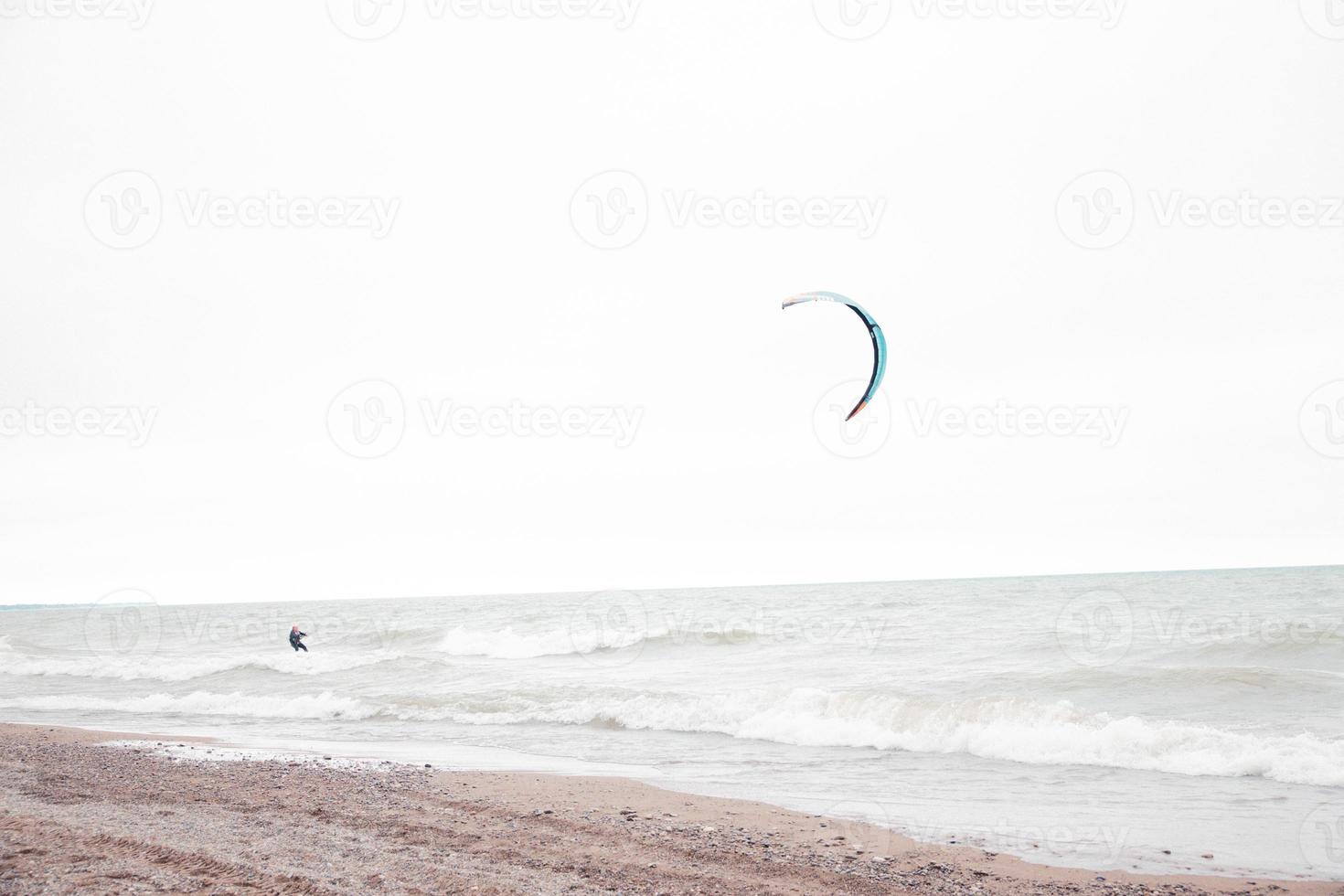 solo kite surf en aguas tormentosas del lago michigan. playa de arena en el borde. pequeños guijarros a lo largo de la línea de la costa. cielo nublado nublado. paracaídas de colores. foto