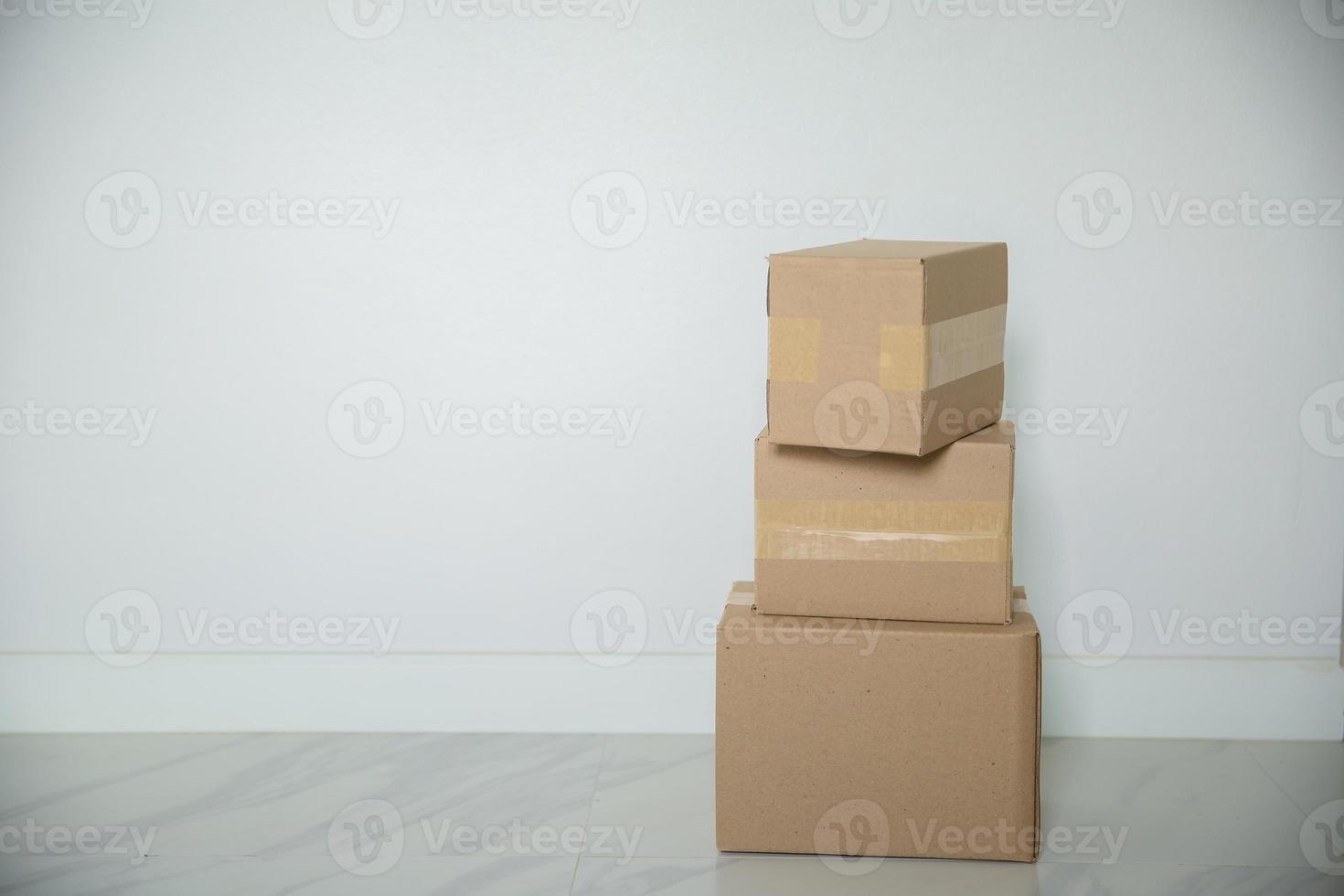 pila de cajas de cartón para mudanzas, habitación vacía con una pared blanca y cajas de cartón con código de barras sin marca en el suelo. entrega de mercancías, compras. cajas de cartón sobre fondo de pared gris. foto