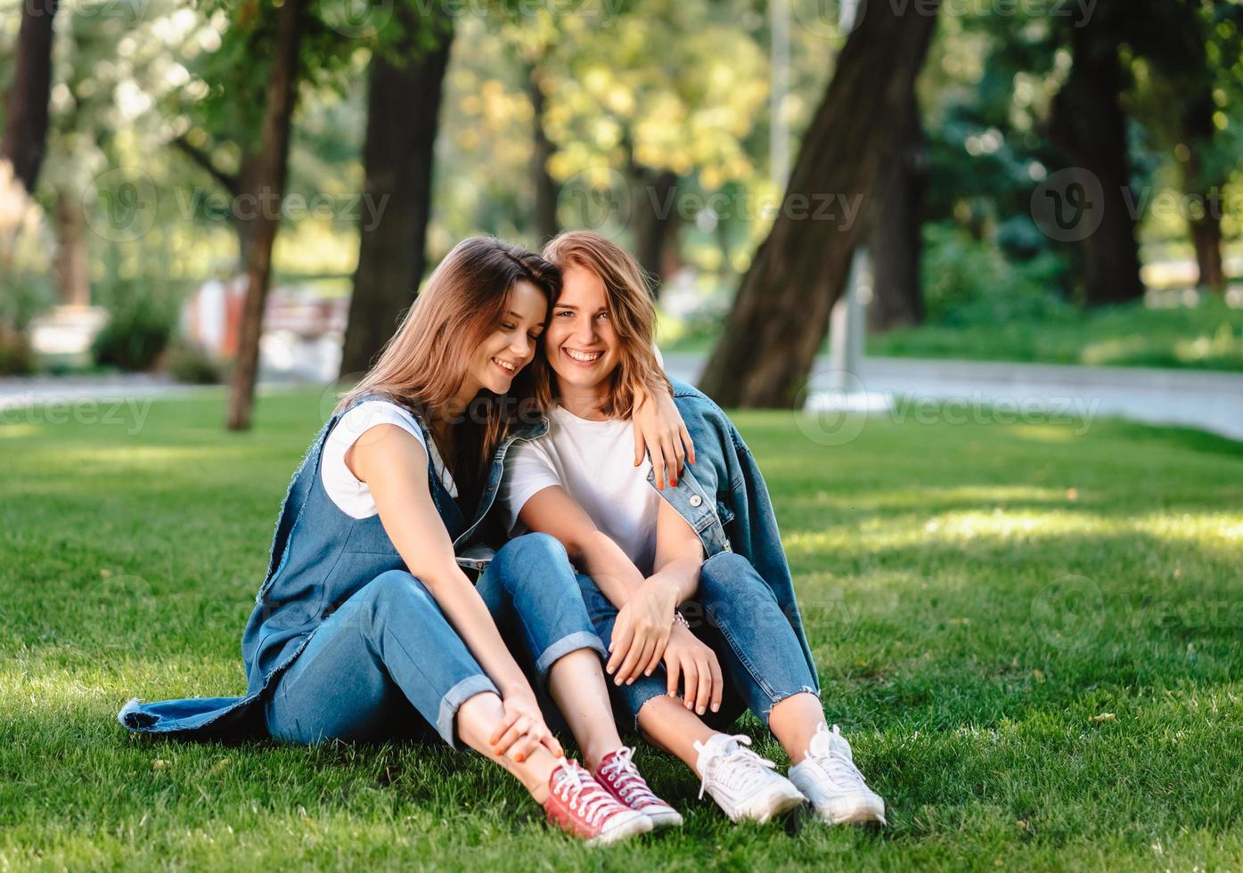 Two friends are sitting on the green lawn in the park. photo