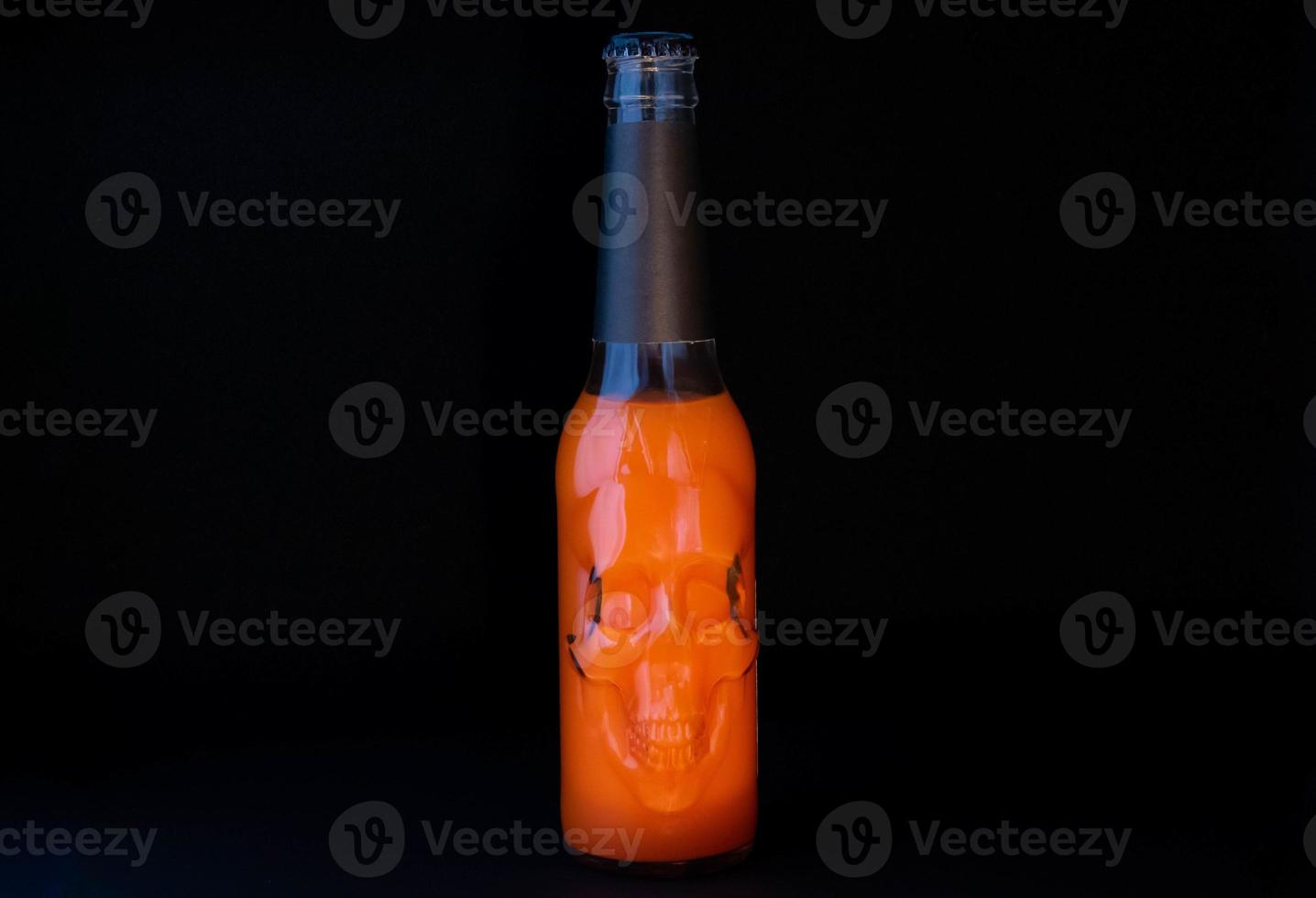 Orange Halloween cocktail in a glass bottle with a skull on a black background. Space for text photo