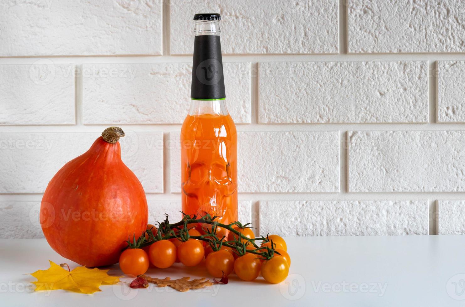 A bottle of orange drink with a skull, ripe pumpkin vegetables and orange cherry tomatoes on a white background.Halloween concept. Place for your text photo