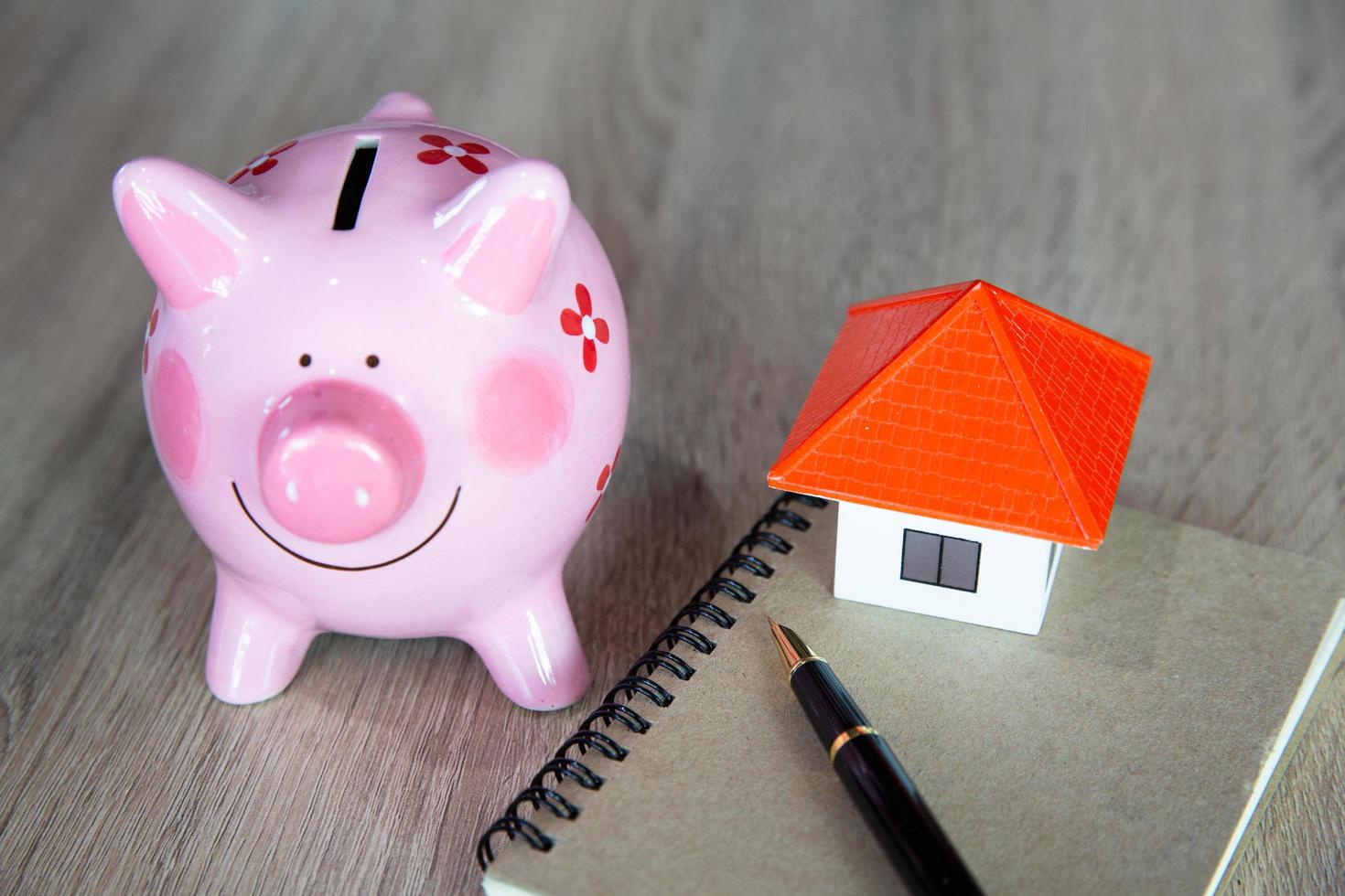 Model of house with Saving book and saving bank pig on wooden table on blurred background. Concept of saving money for buying a house and residence. photo