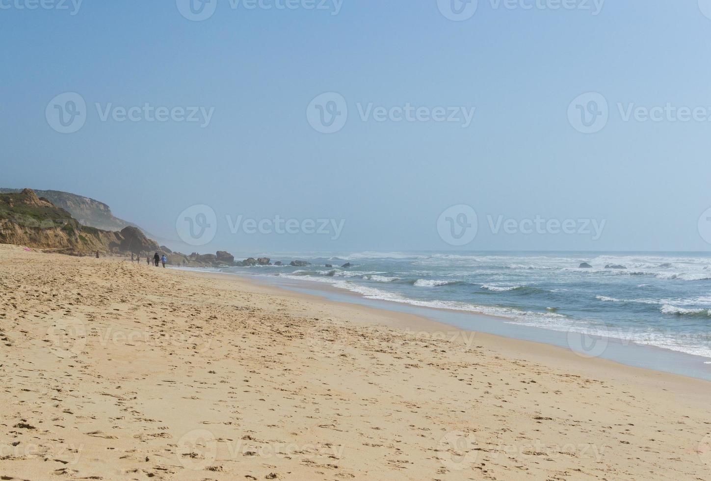 Beach by the ocean with people resting, vacation spot. Mountains, sea and waves. Travel to Europe Portugal. photo