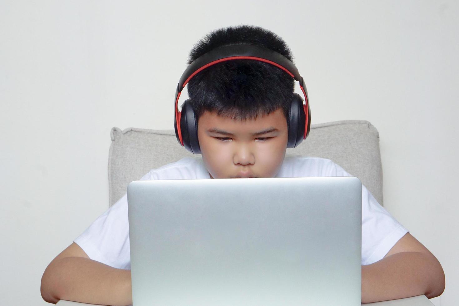 The boy sit on sofa is using laptop and wearing headphones. Education, learning and technology concept. photo