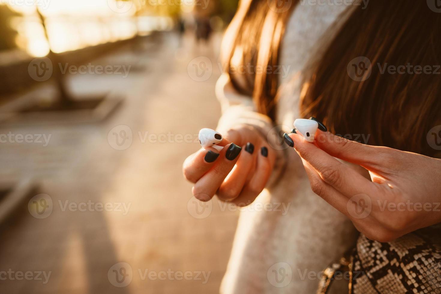 Beautiful young girl holding wireless headphones in park photo