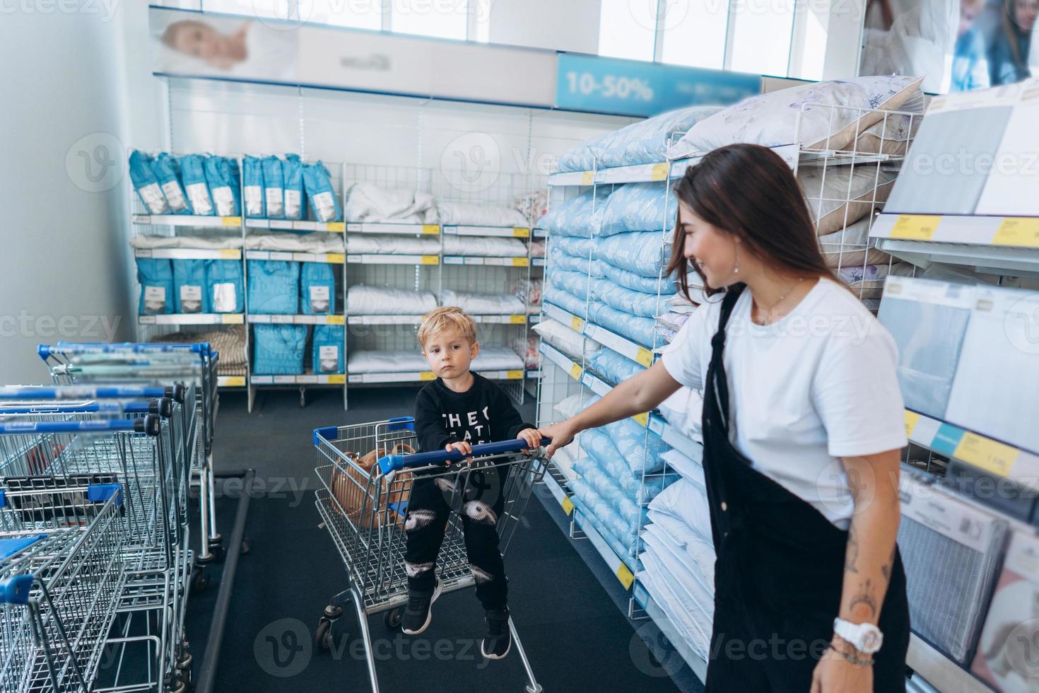 Beautiful mother carries her little son in the supermarket trolley photo