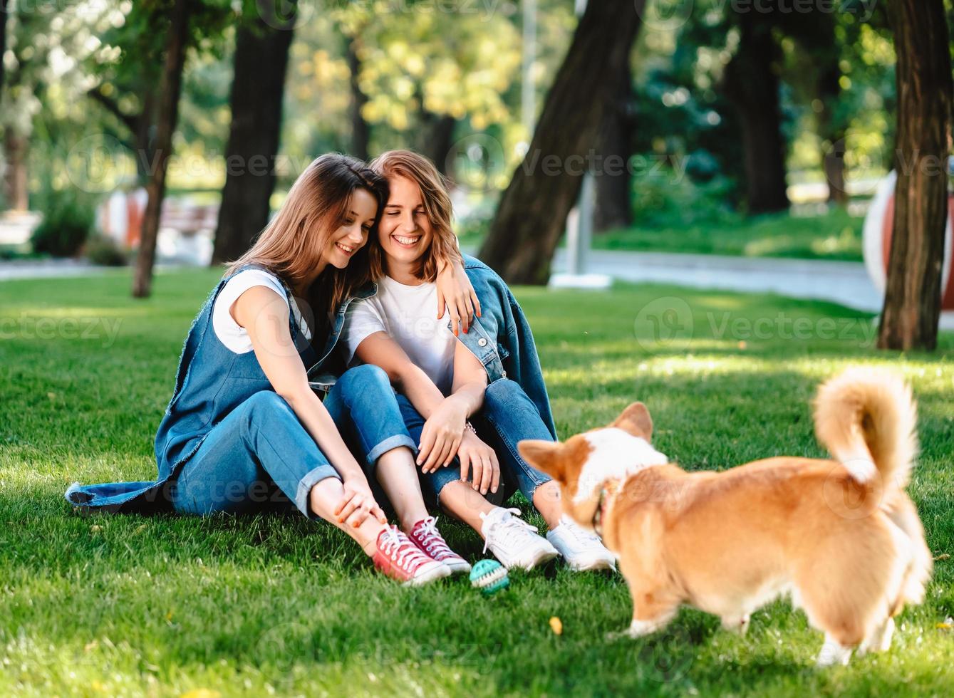 Two female friend in the park play with little dog photo