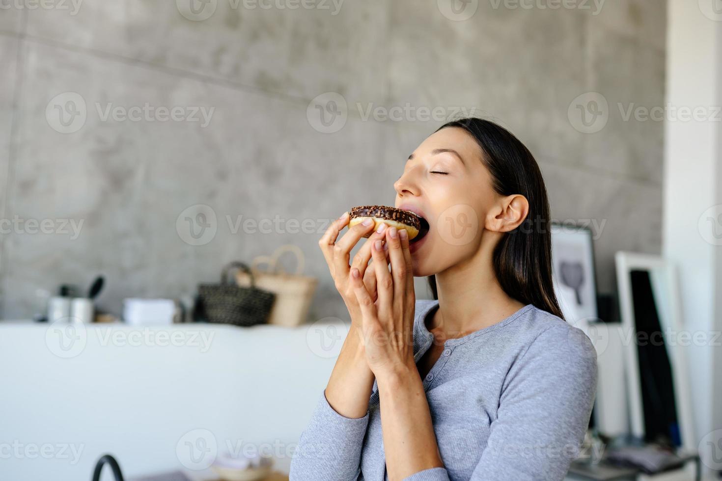 Portrait of rejoicing woman eats tasty donut at home. photo