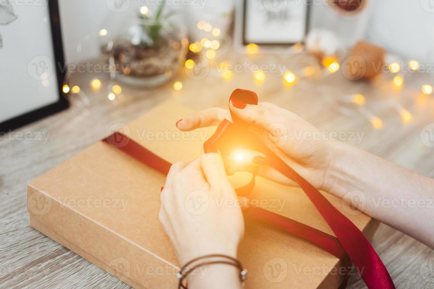 Woman wrapping present in paper with red ribbon. photo