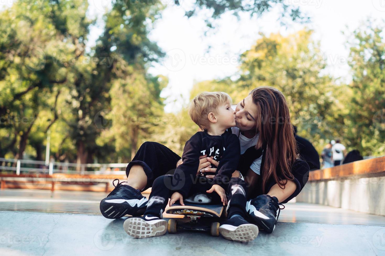 joven madre le enseña a su hijo pequeño a andar en patineta foto