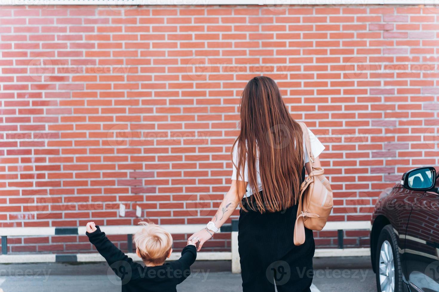 vista trasera de la madre y su pequeño hijo contra el telón de fondo de una pared de ladrillos foto