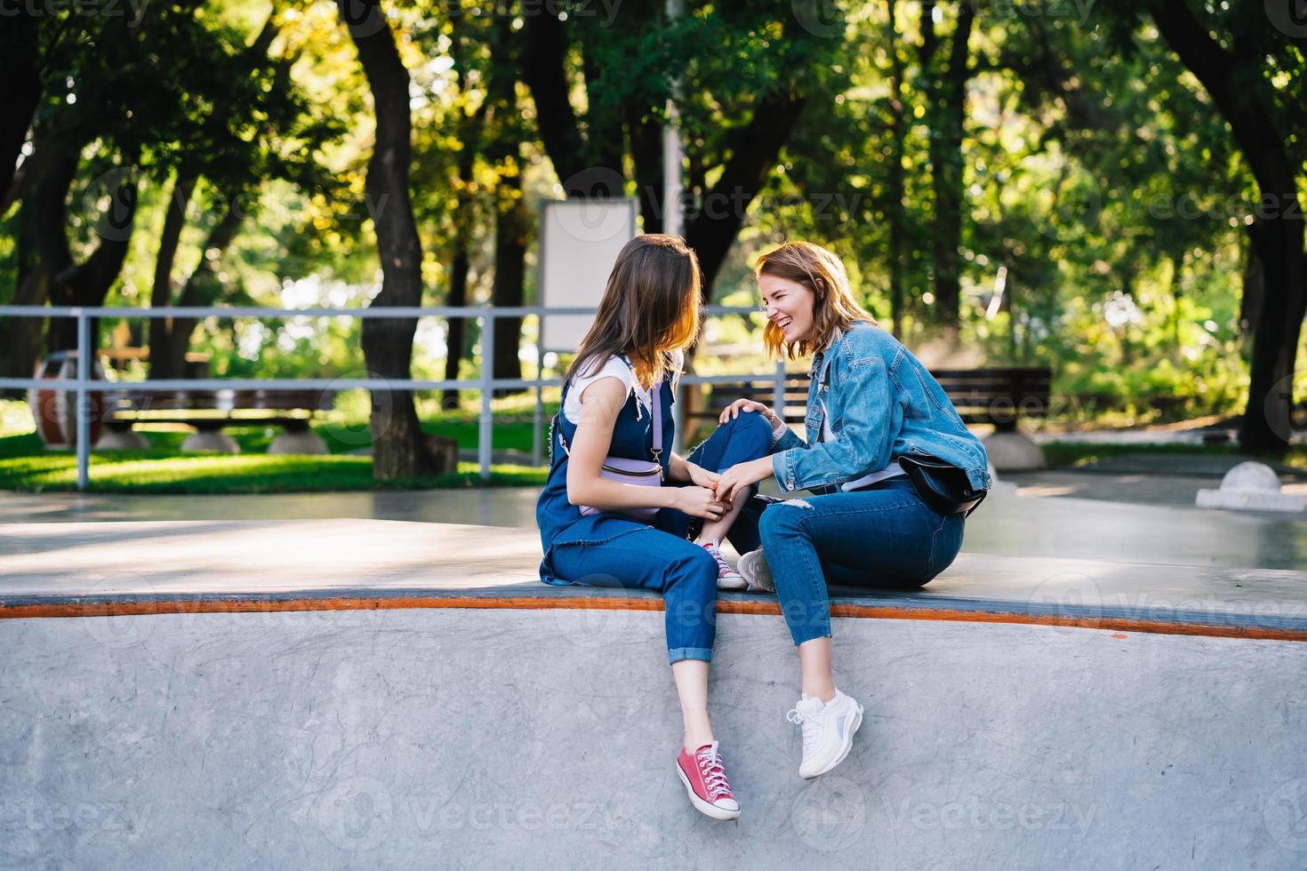 Two happy young girls sitting at the skate park photo