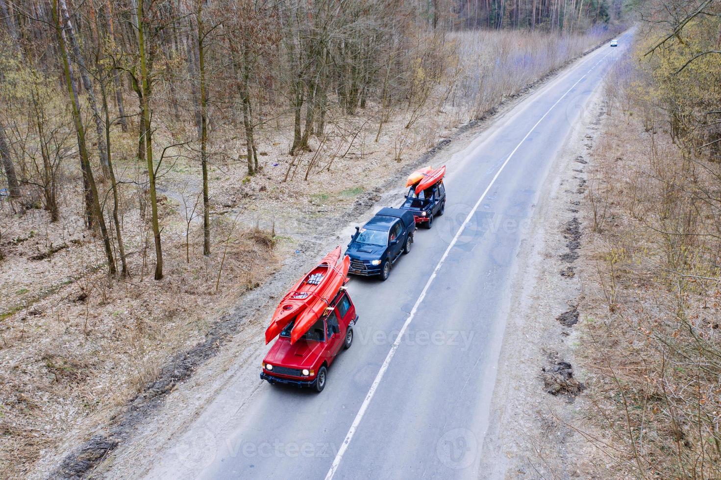 Several cars with kayaks on roof rack driving on the road among trees photo