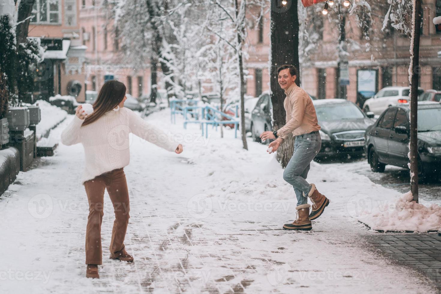 Joyful young couple is playing snowballs at the street. photo