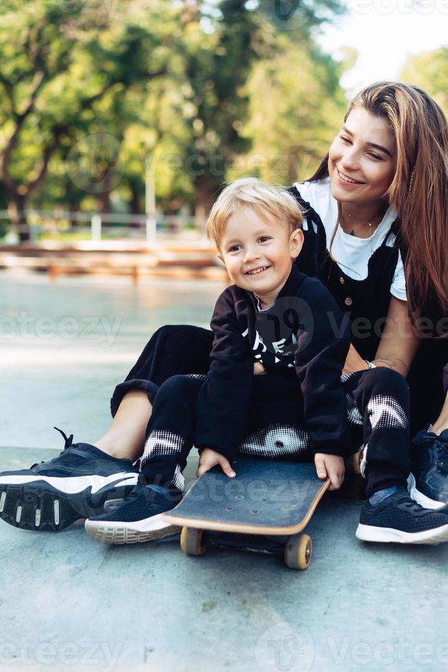 Young mother teaches her little boy to ride a skateboard photo