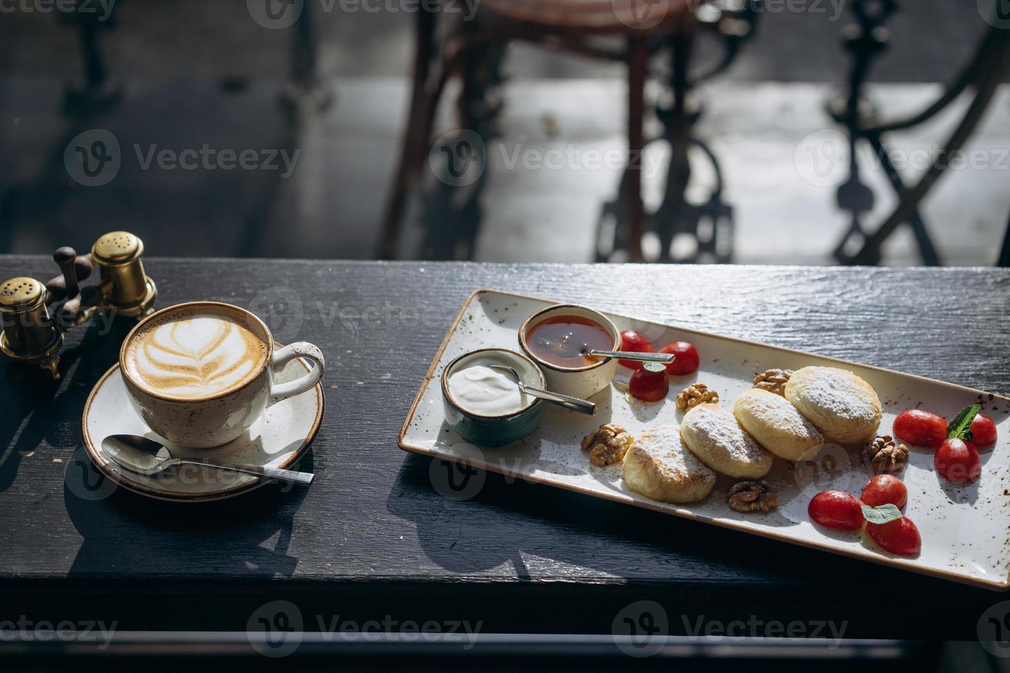 tortitas de requesón con crema agria, miel en una bandeja y café con leche foto