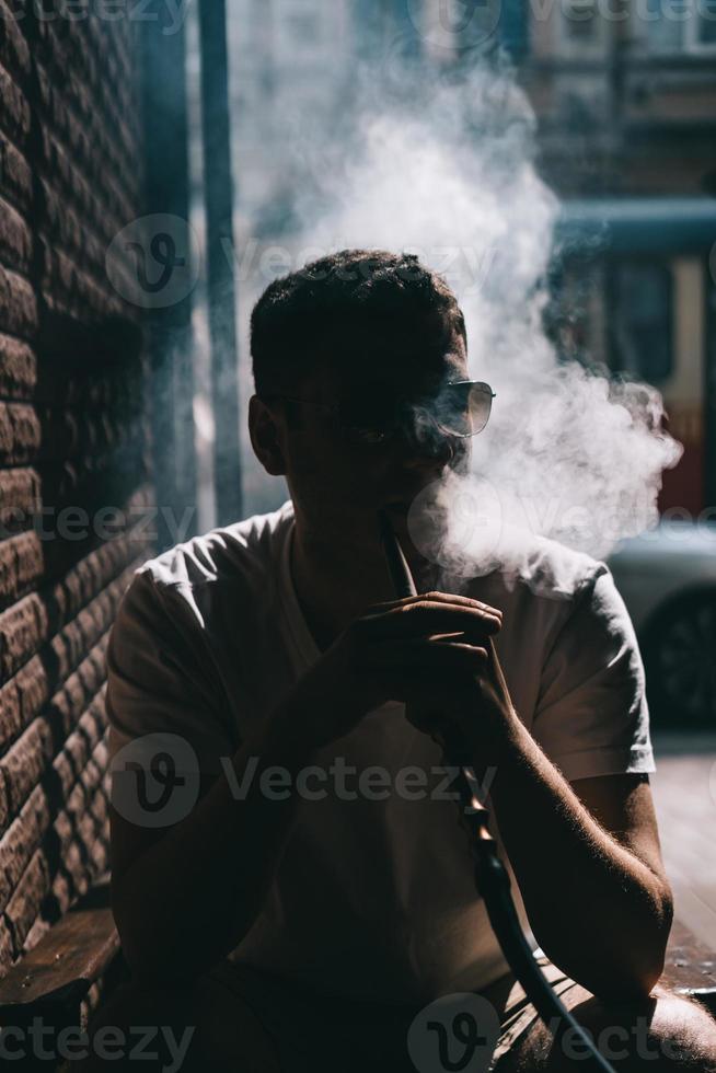 silueta del fabricante de narguiles que sopla humo en la oscuridad. foto