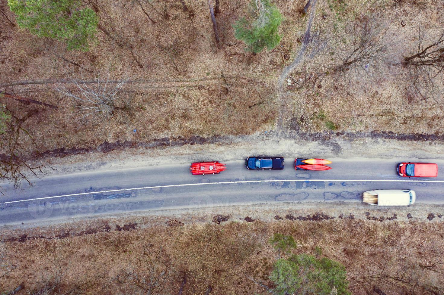 Several cars with kayaks on roof rack driving on the road among trees photo