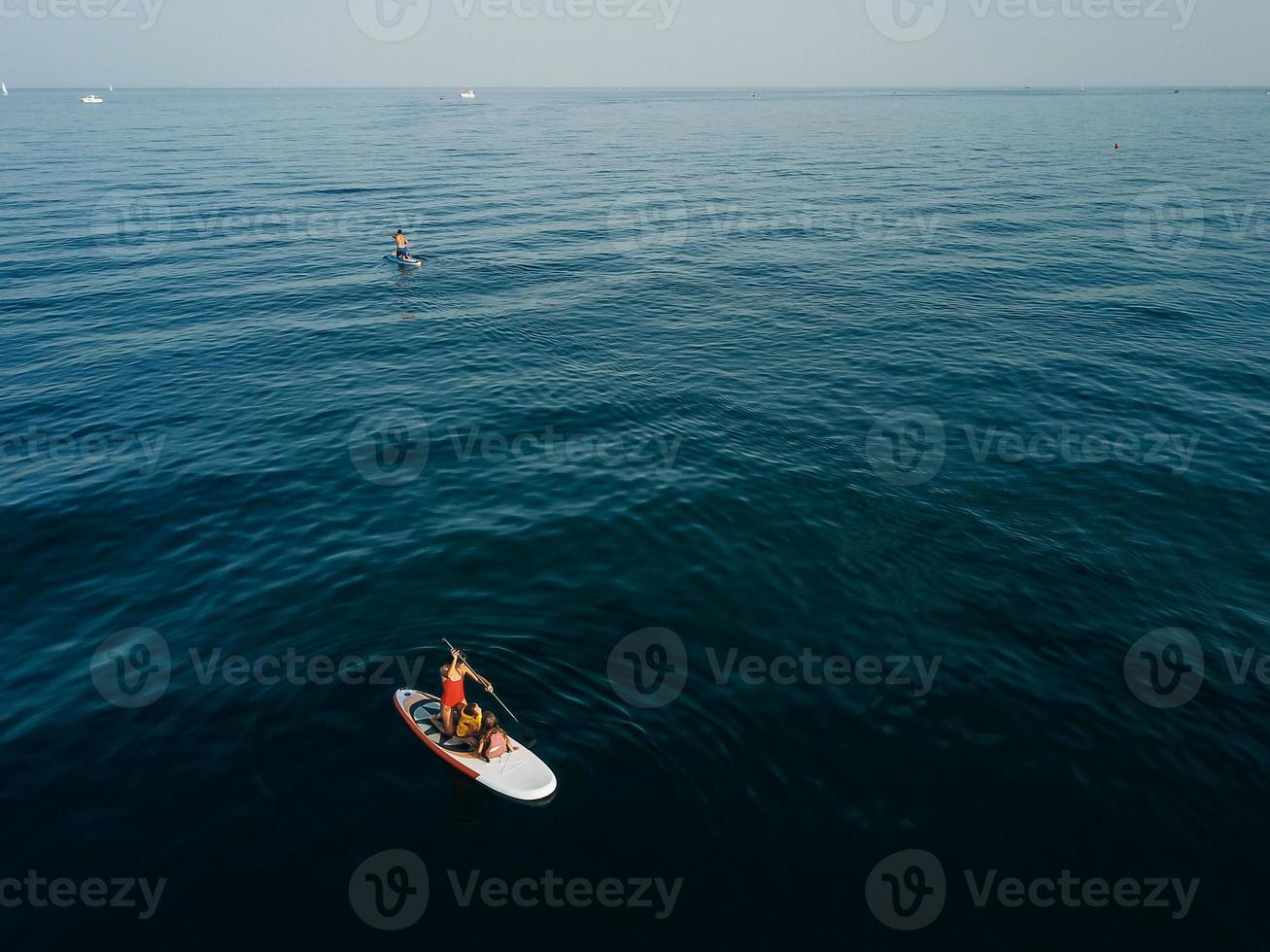 Mother with two daughters stand up on a paddle board photo